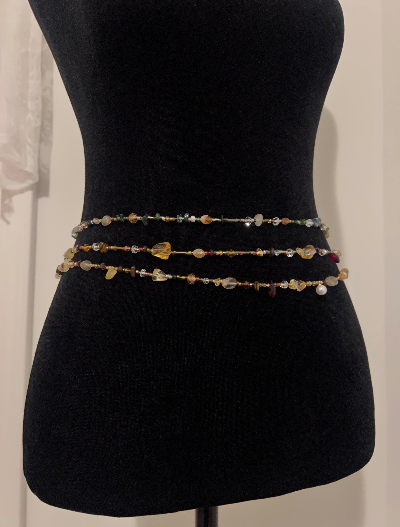 Handmade beaded waist chain with colorful gemstones and pearls displayed on a black mannequin.