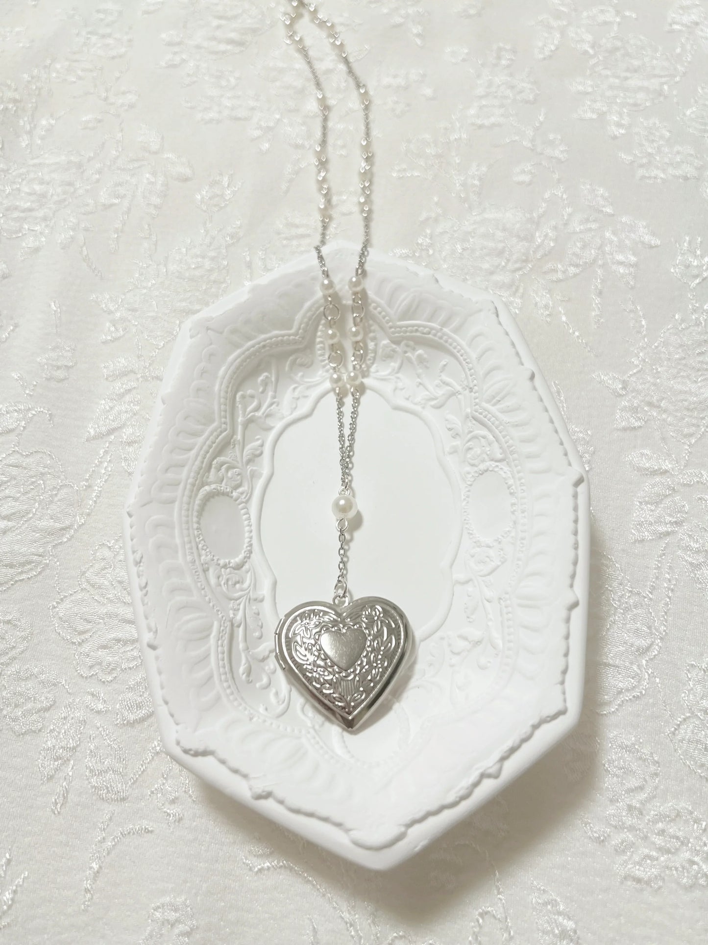 Silver heart locket necklace with pearls on white decorative tray, handmade jewelry accessory
