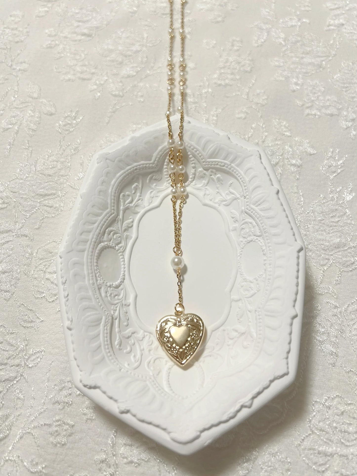 Gold heart locket necklace with pearls on ornate white dish, handmade jewelry accessory