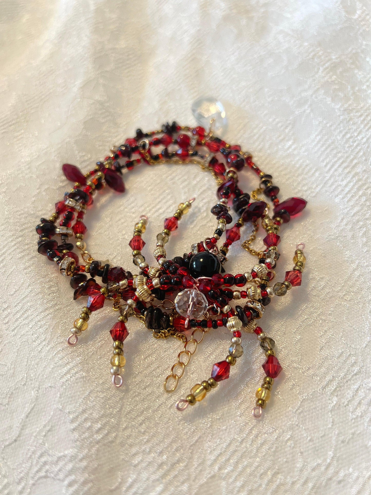 Handmade beaded necklace with red, black, and gold beads, featuring a central black bead and crystal accents on white fabric.