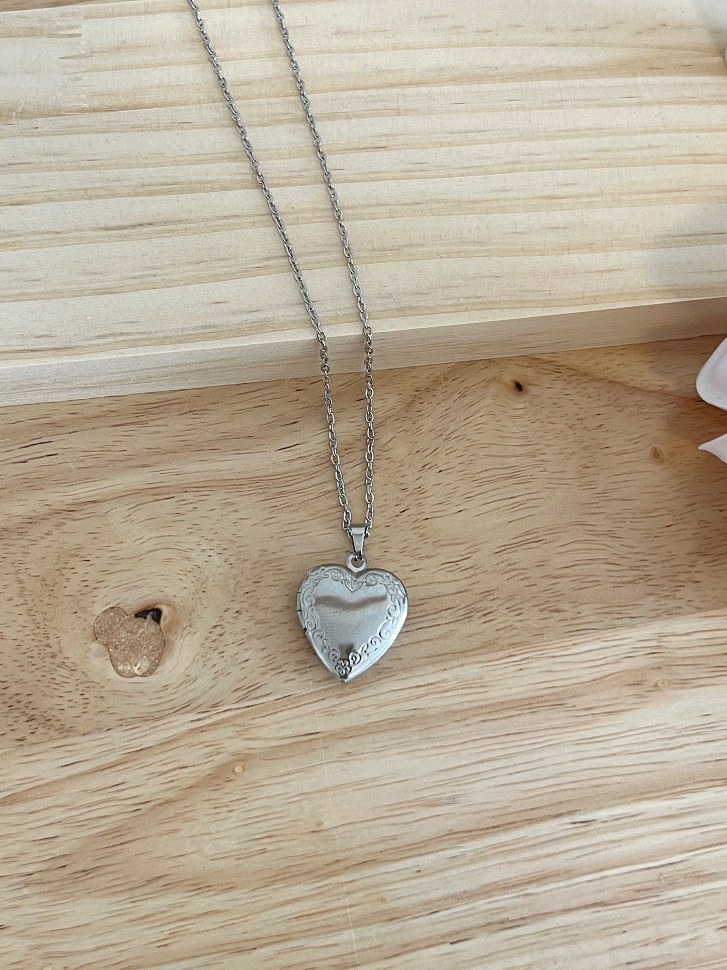 Silver heart locket necklace with intricate scrollwork, displayed on light wood surface.