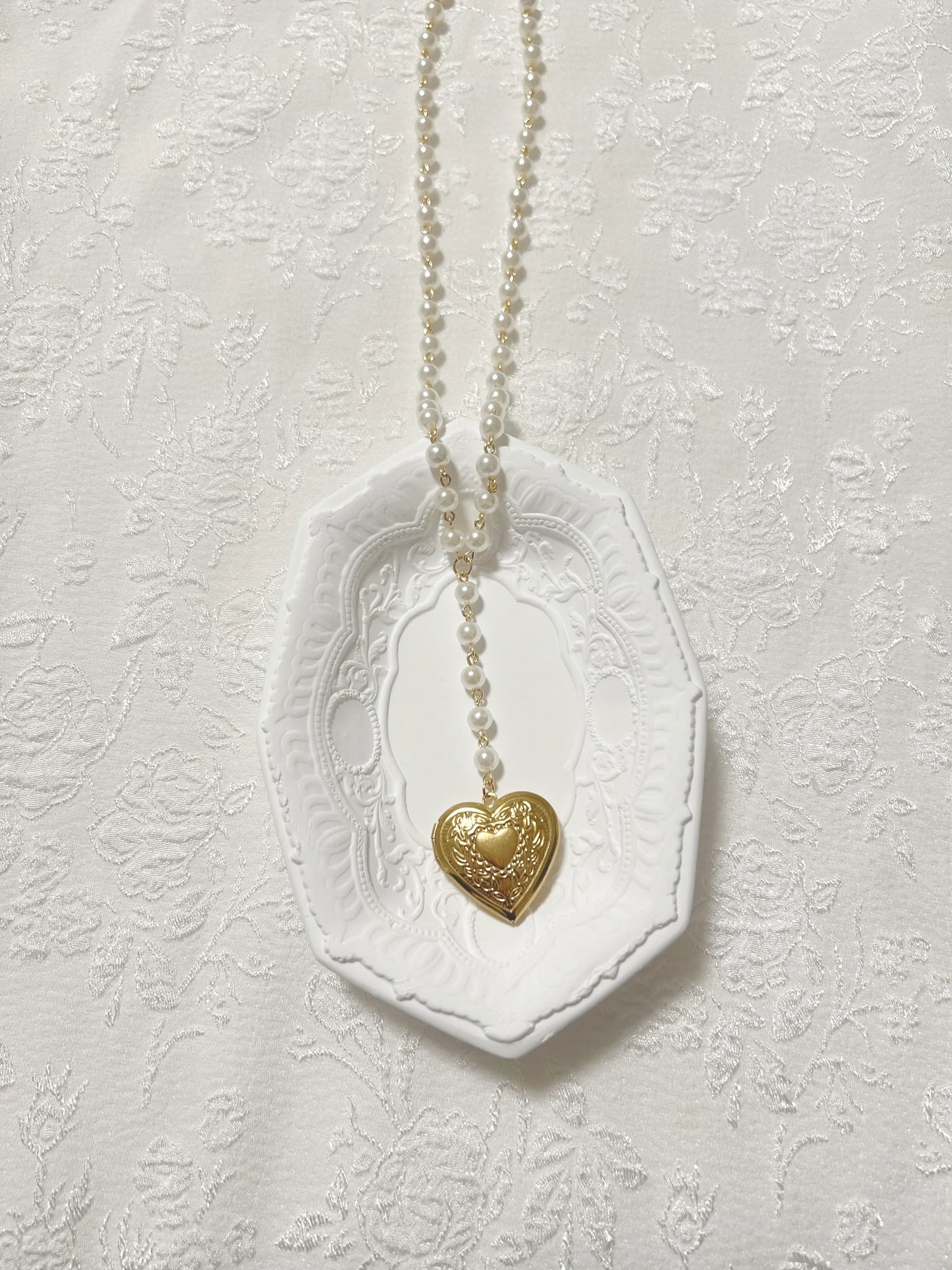 Gold heart locket necklace with pearl chain on white decorative tray, elegant handmade jewelry