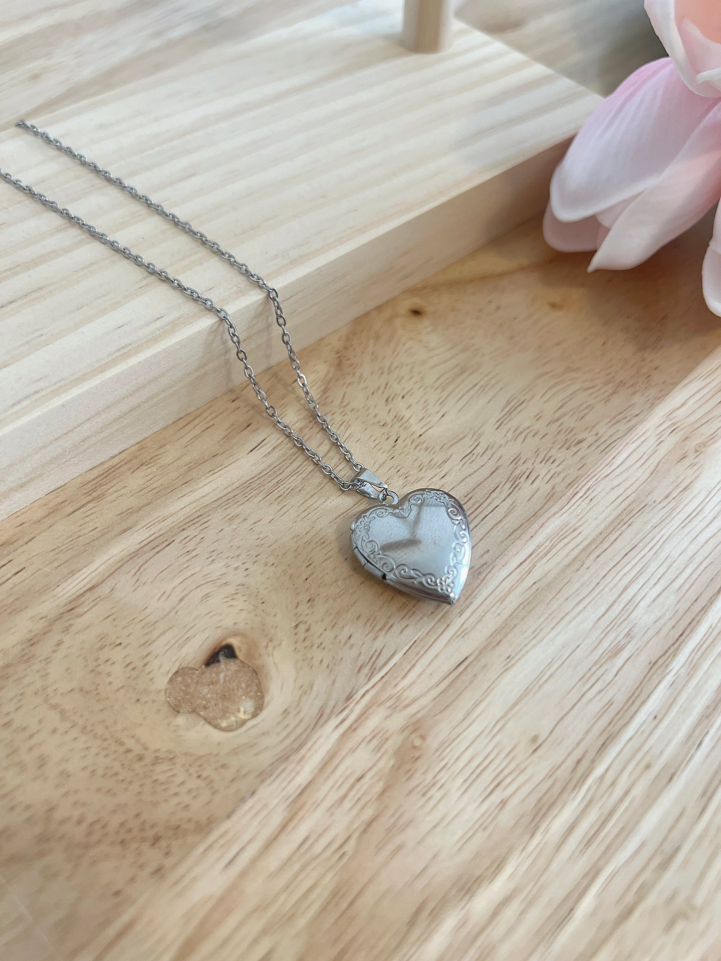 Heart-shaped locket necklace with intricate design on wooden surface