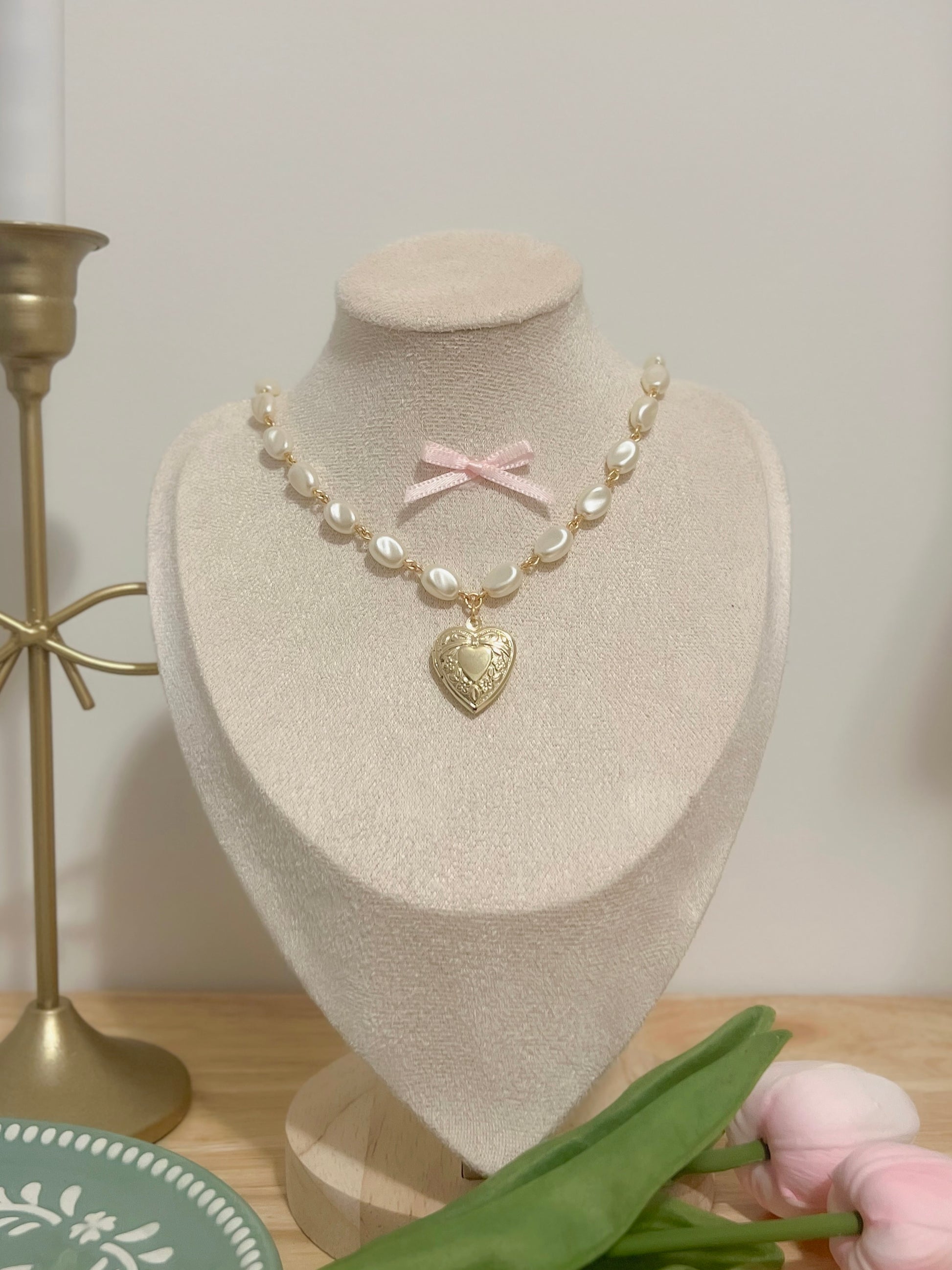 Elegant pearl necklace with gold heart locket and pink bow, displayed on a mannequin.