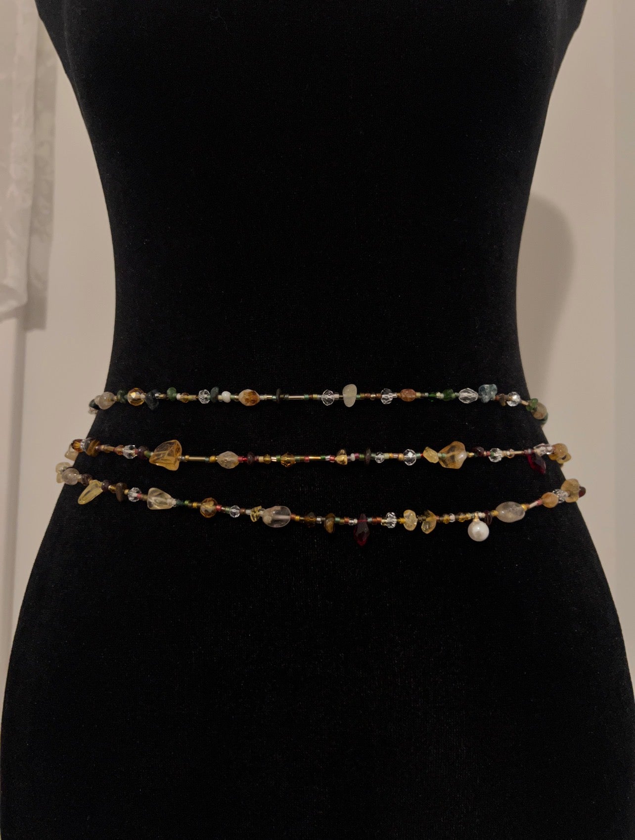 Handmade beaded waist chain with colorful gemstones and pearls, displayed on a black mannequin.