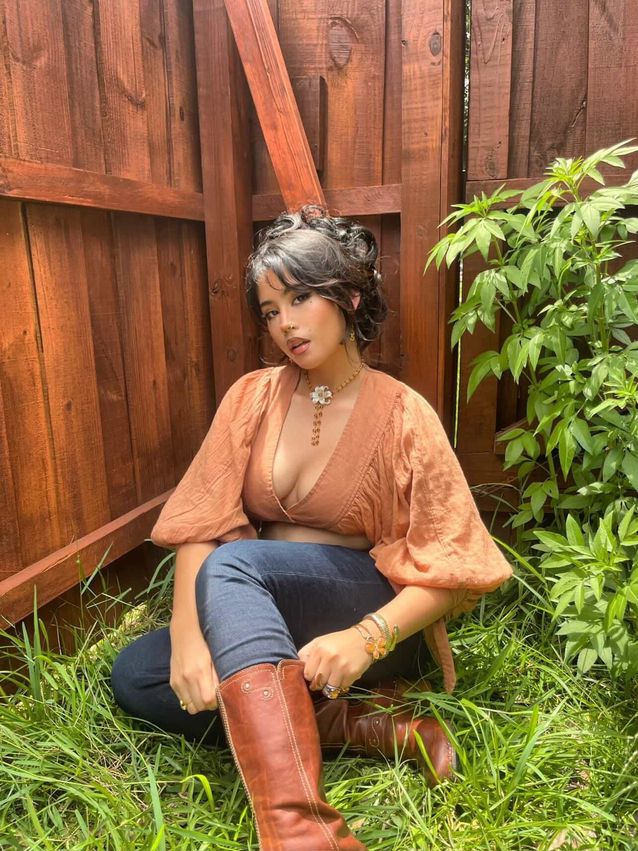 Woman wearing handmade floral necklace and boho jewelry, sitting in grass near wooden fence