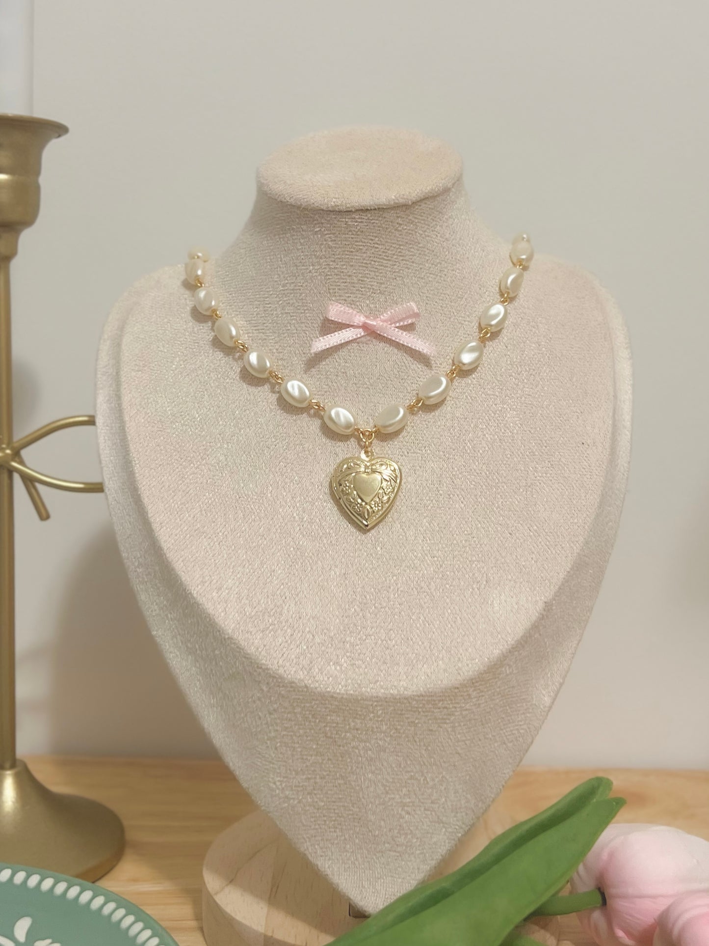 Elegant pearl necklace with gold heart locket and pink bow, displayed on a mannequin.