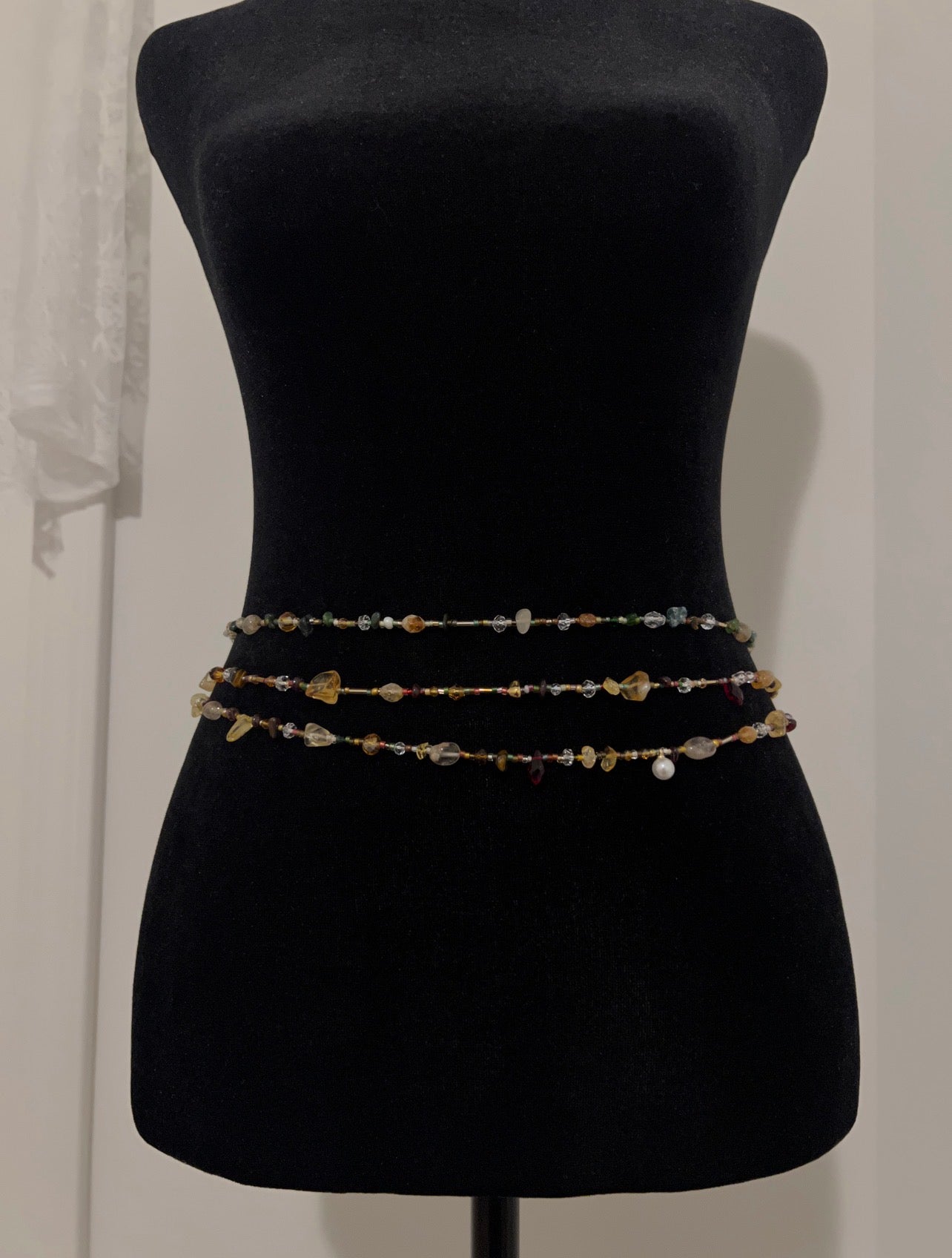 Handmade waist beads with colorful gemstones displayed on a black mannequin.