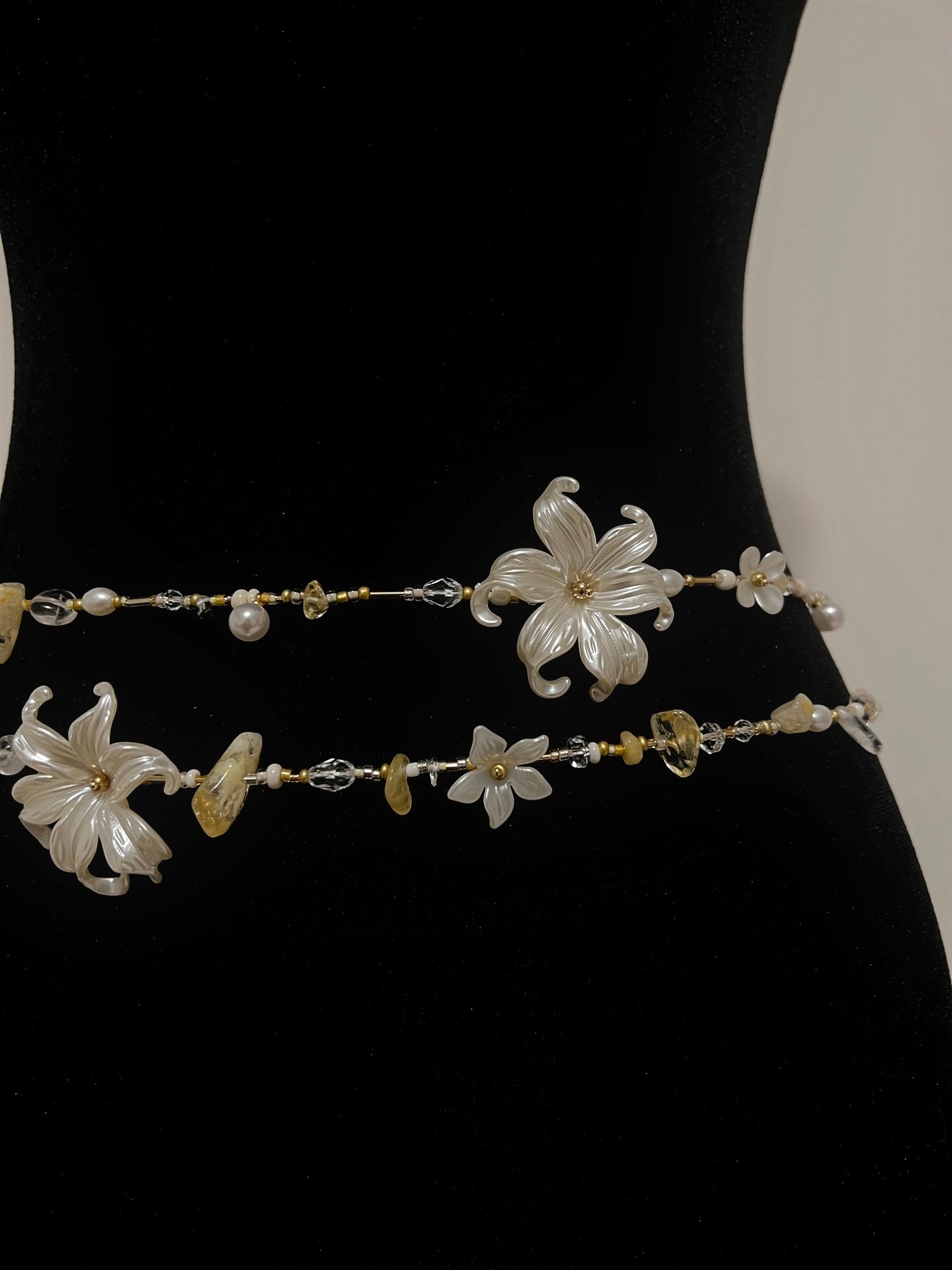 Handmade floral waist bead with pearls, crystals, and gold accents on black display