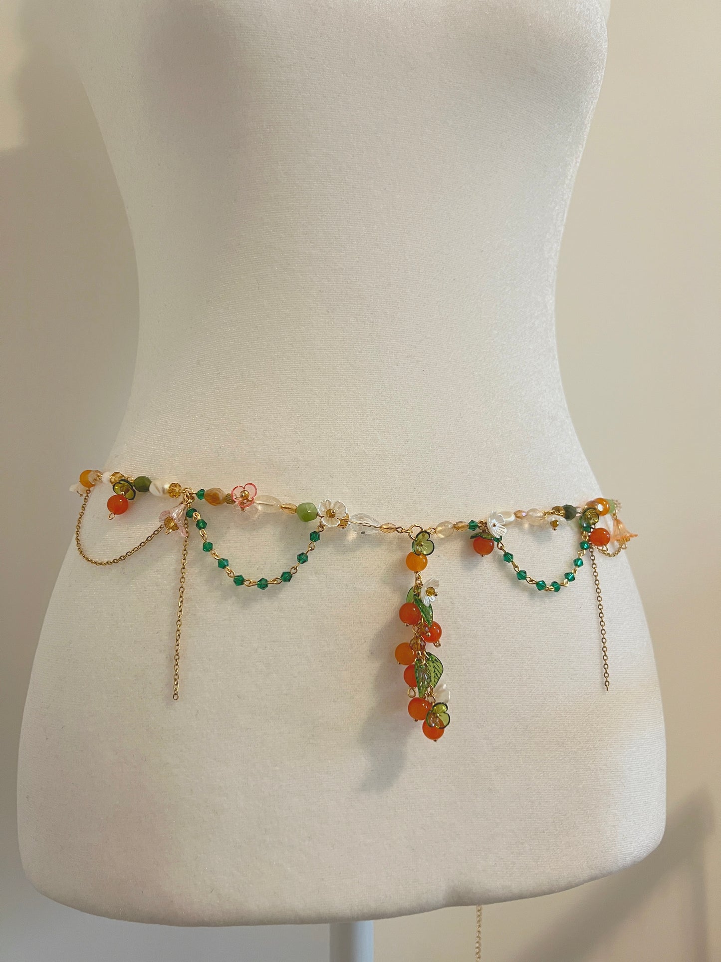 Handmade waist bead with orange, green beads, and floral charms on a mannequin