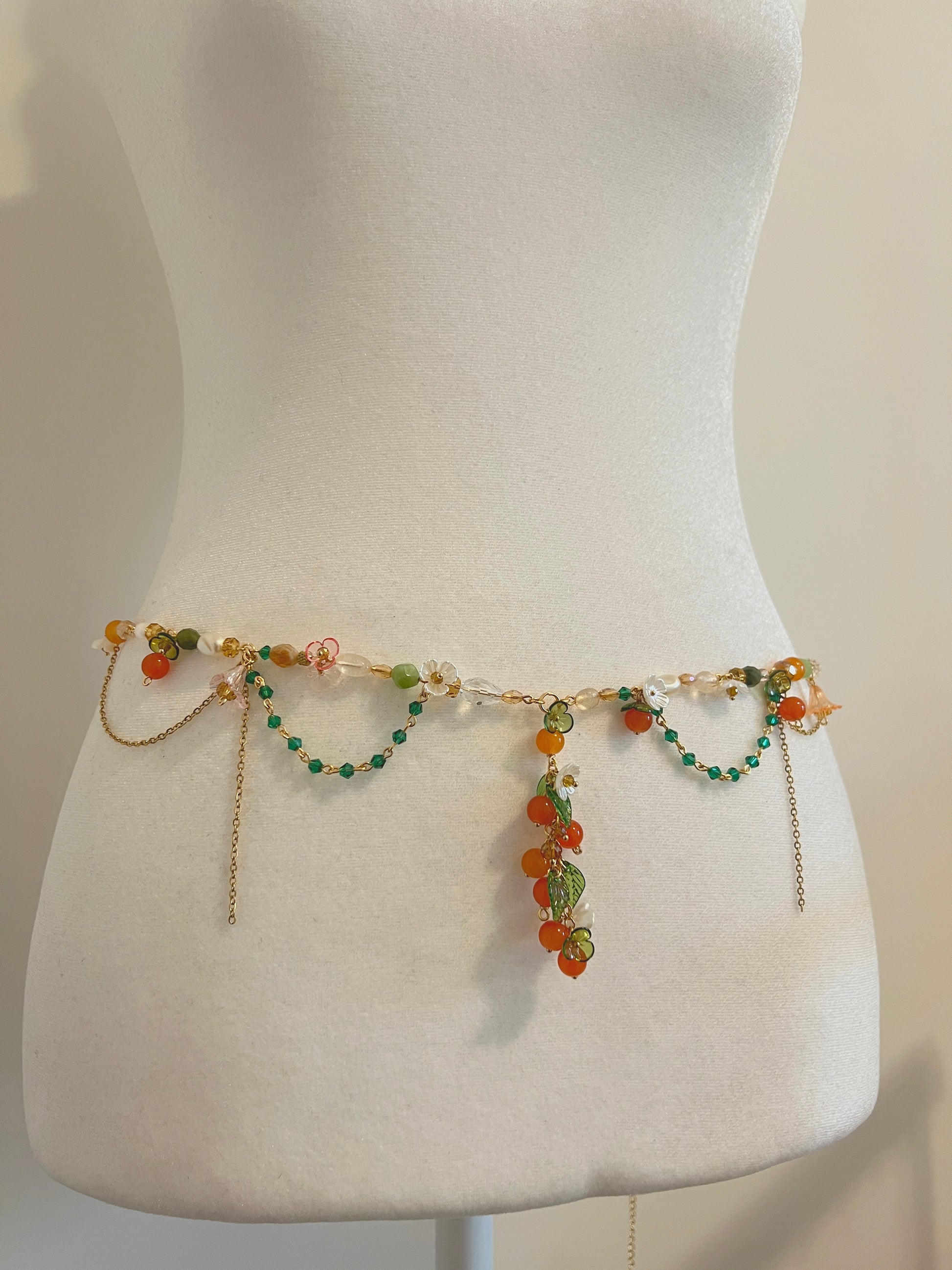 Handmade waist bead with orange, green beads, and floral charms on a mannequin