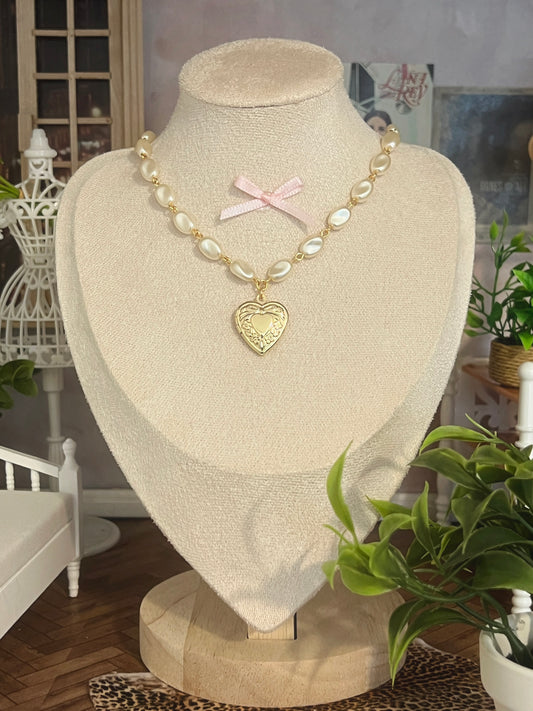 Elegant pearl necklace with gold heart locket and pink bow, displayed on a mannequin.