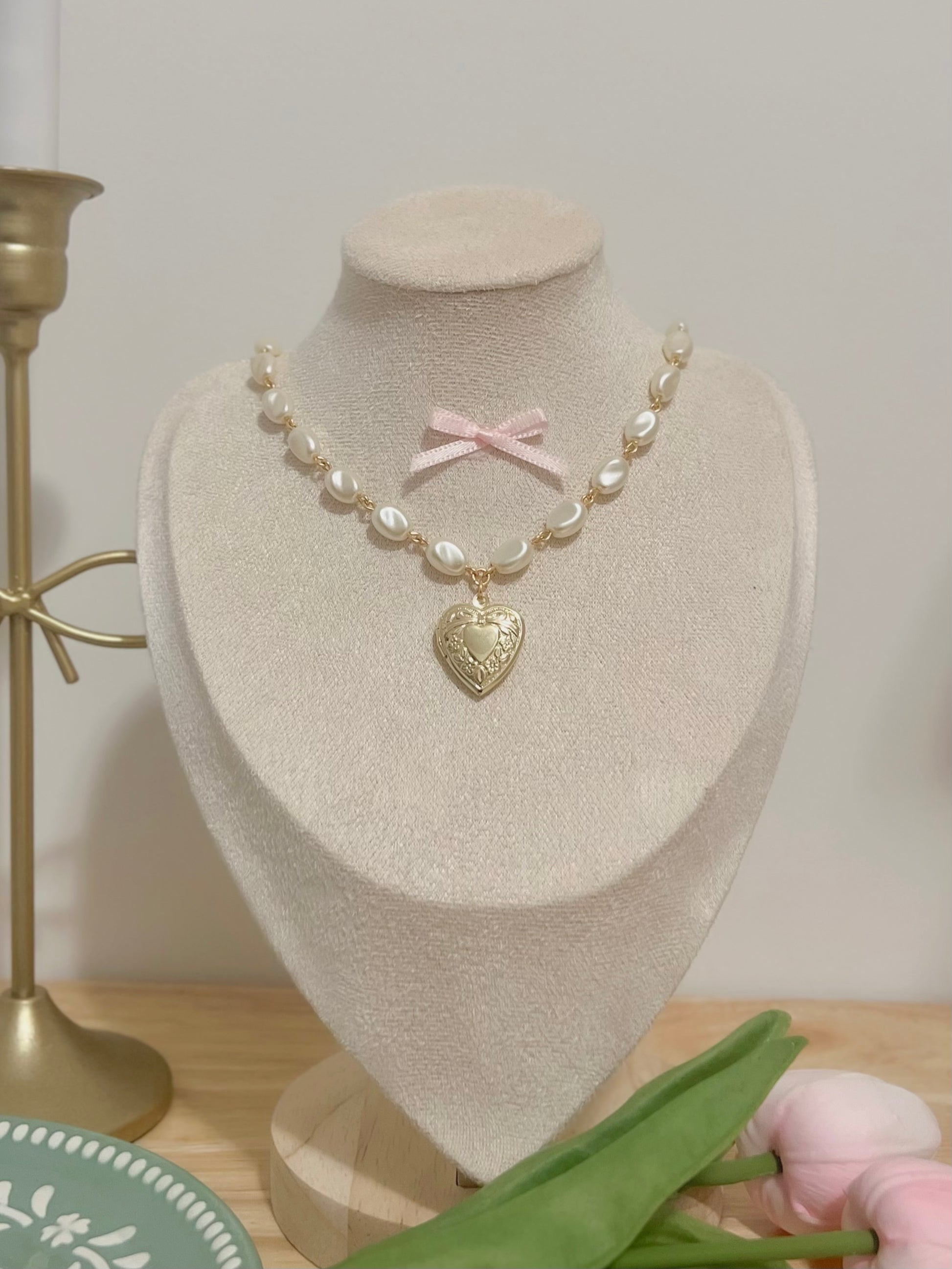 Elegant pearl necklace with heart locket and pink bow, displayed on a mannequin.