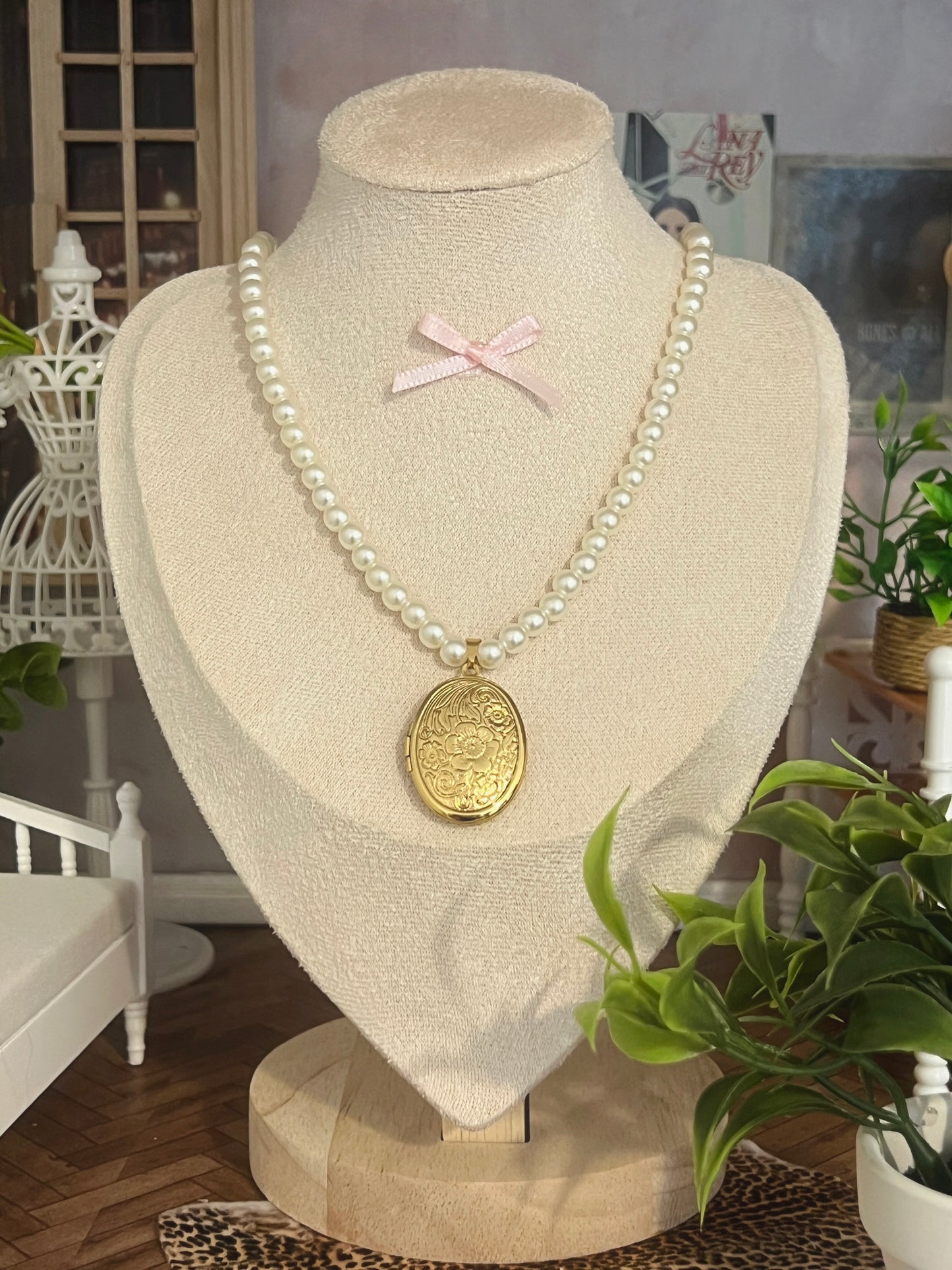 Elegant pearl necklace with gold floral locket, displayed on mannequin with pink bow accent.