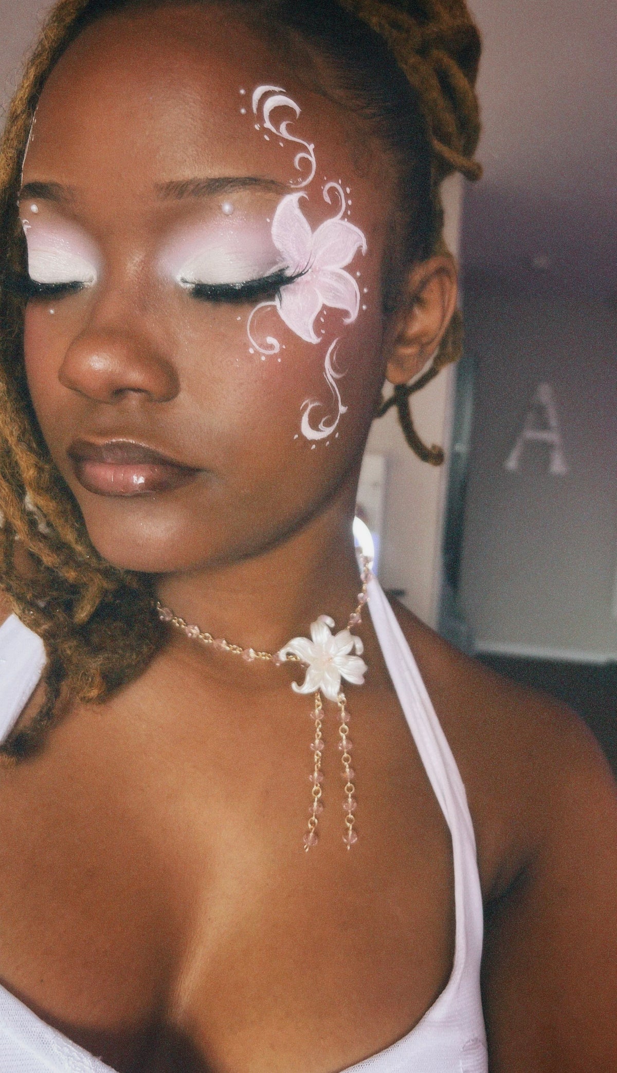 A close-up lifestyle shot of a woman with white and pink floral face paint, wearing a white halter top and a silver-toned floral choker necklace.