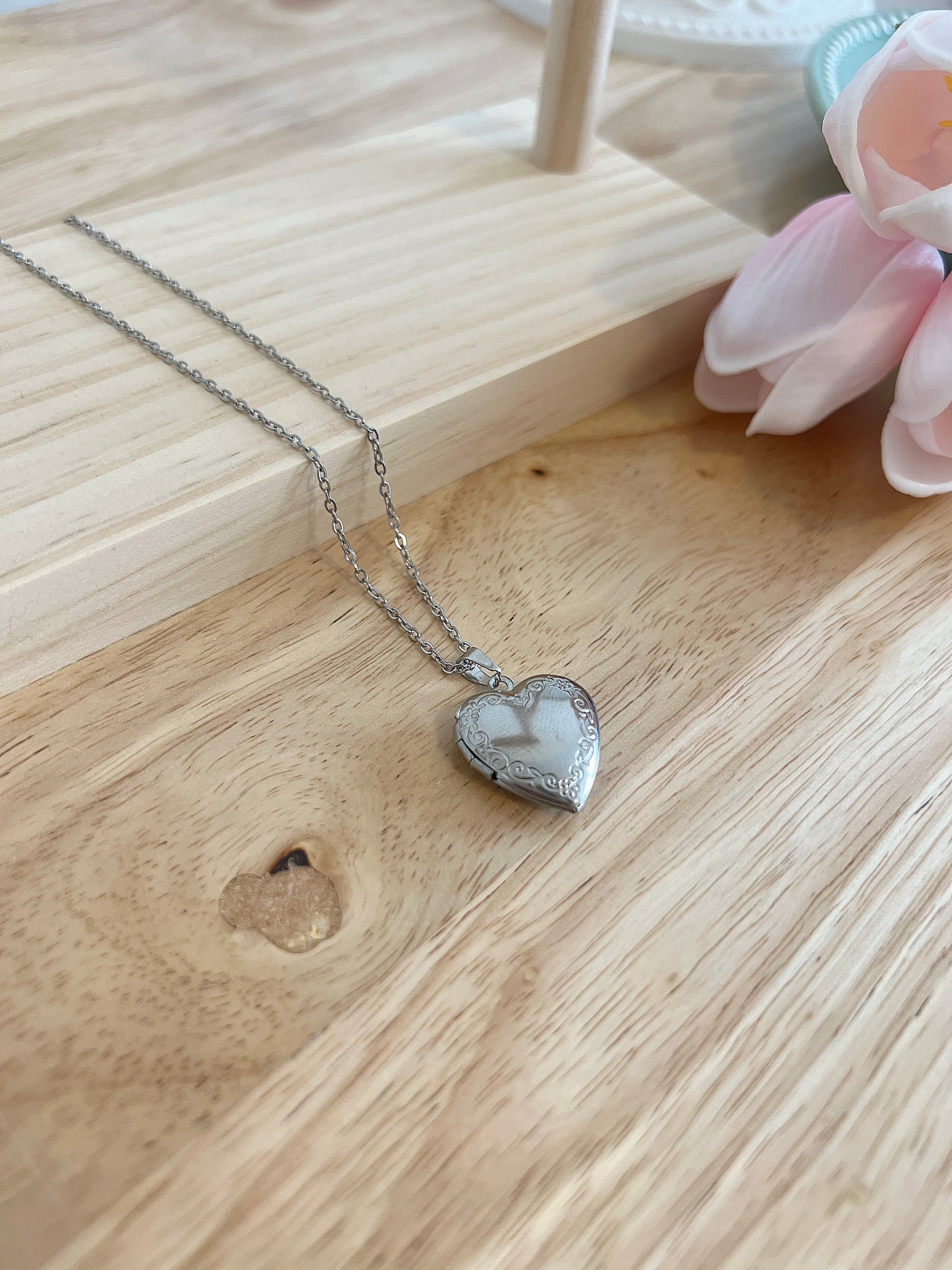 Heart-shaped locket necklace on wooden surface with pink flower accent