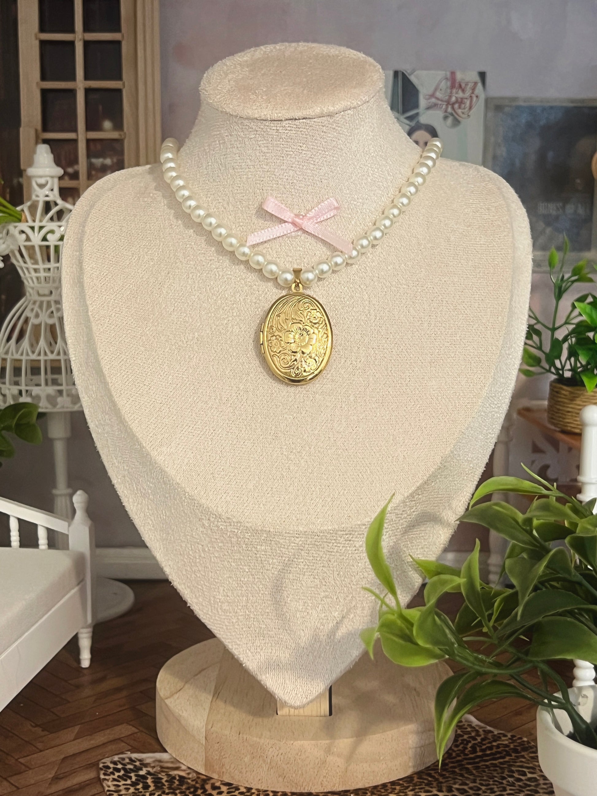 Elegant pearl necklace with gold floral locket and pink ribbon accent, displayed on mannequin.